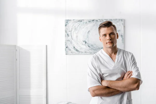 Masseur standing with crossed arms and looking at camera in clinic — Stock Photo