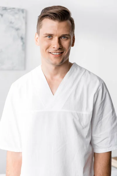 Vue de face du masseur souriant regardant la caméra à la clinique — Photo de stock