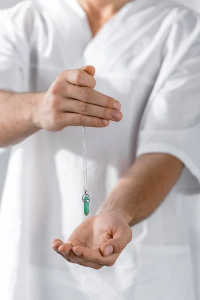 Cropped view of hypnotist holding green stone in clinic — Stock Photo