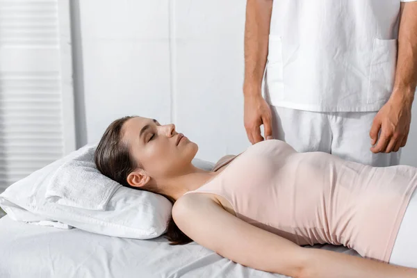 Cropped view of masseur standing near woman lying on massage table with closed eyes — Stock Photo