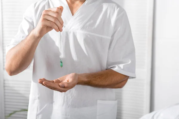 Cropped view of hypnotist holding green stone in clinic — Stock Photo