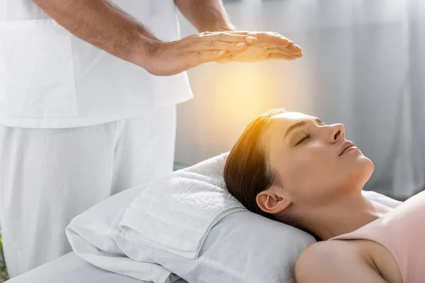 Vista cortada de curandeiro em pé perto do paciente na mesa de massagem e limpeza aura — Fotografia de Stock