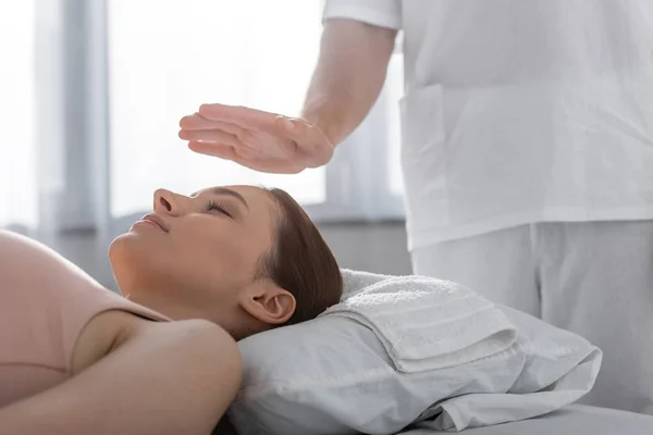 Vista cortada de curandeiro em pé perto do paciente na mesa de massagem e limpeza aura — Fotografia de Stock