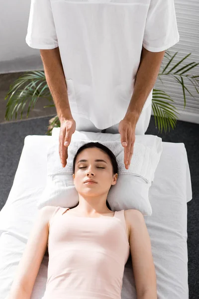 Vue recadrée du guérisseur debout près du patient sur la table de massage et l'aura de nettoyage — Photo de stock