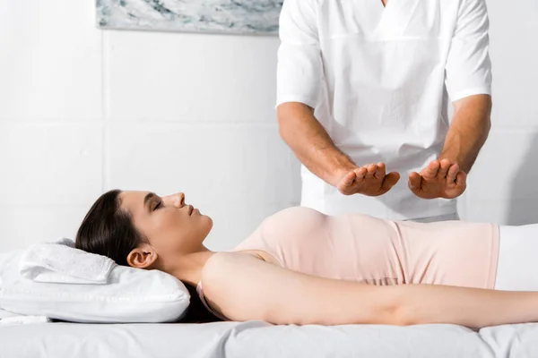 Vista recortada del sanador de pie cerca de la mujer y cogido de la mano por encima de su estómago - foto de stock