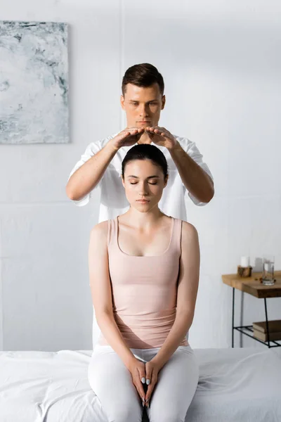 Jovem mulher sentada com os olhos fechados enquanto curandeiro limpeza sua aura — Fotografia de Stock