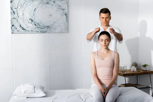 Jeune femme assise les yeux fermés tandis que guérisseur nettoyer son aura — Photo de stock