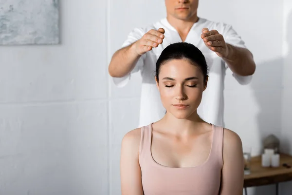 Vista recortada del sanador de pie cerca de la mujer con los ojos cerrados y sosteniendo las manos por encima de su cabeza - foto de stock