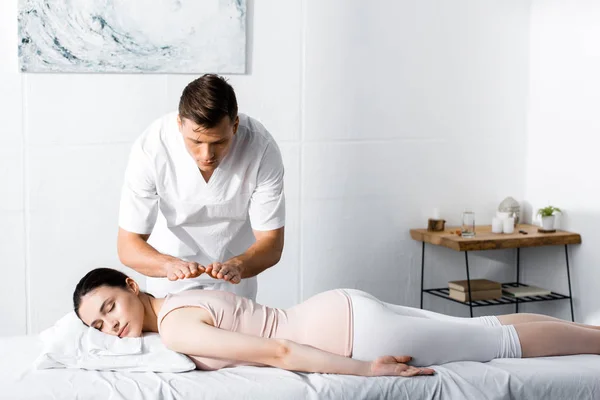 Focused healer standing near woman lying on massage table with closed eyes and holding hands above her body — Stock Photo