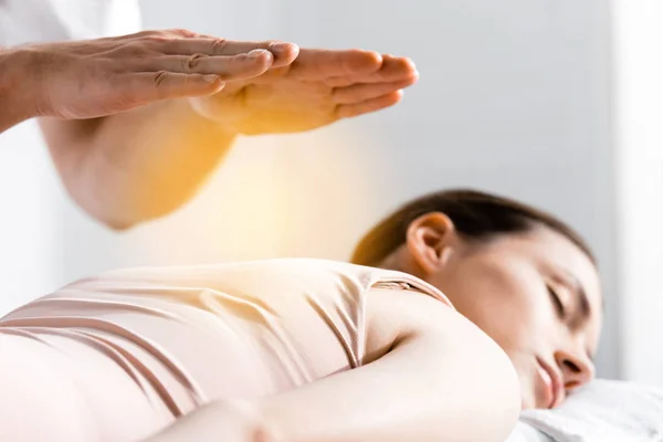 Cropped view of healer standing near woman lying with closed eyes and holding hands above her body — Stock Photo