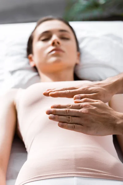 Vista recortada del sanador de pie cerca de la mujer acostada con los ojos cerrados y sosteniendo las manos sobre su cuerpo - foto de stock