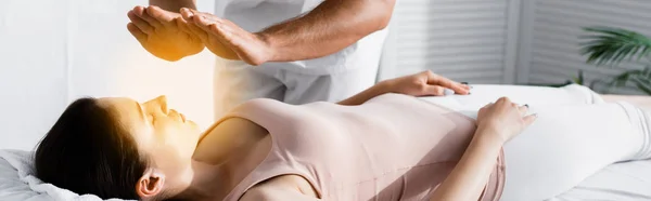 Tiro panorâmico de vista cortada de curandeiro em pé perto da mulher na mesa de massagem e limpeza de sua aura — Fotografia de Stock