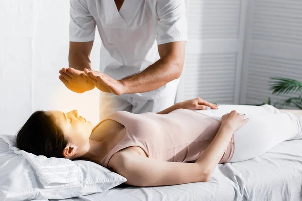 Vista cortada de curandeiro em pé perto da mulher na mesa de massagem e limpeza de sua aura — Fotografia de Stock