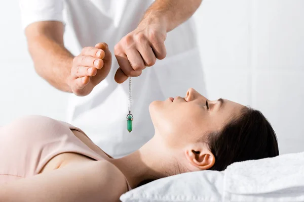 Cropped view of hypnotist standing near woman on pillow and holding green stone — Stock Photo