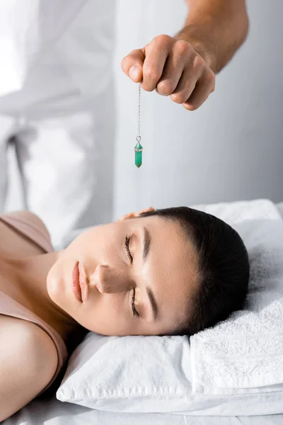 Vista recortada de hipnotizador de pie cerca de la mujer en la almohada y la celebración de piedra verde - foto de stock