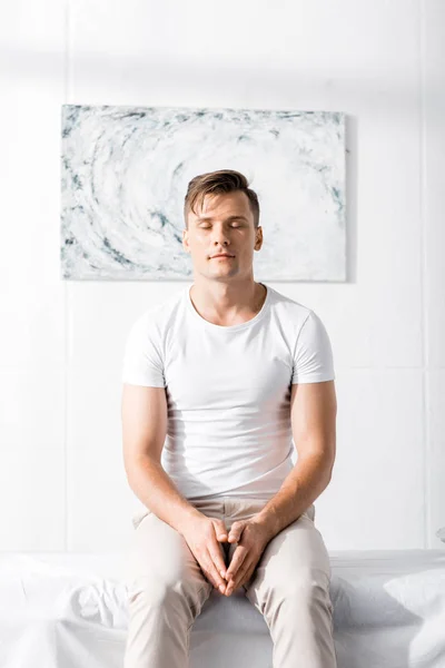 Front view of man in white t-shirt sitting on massage table with closed eyes in clinic — Stock Photo