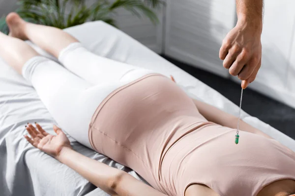 Cropped view of hypnotist standing near woman on massage table and holding green stone — Stock Photo
