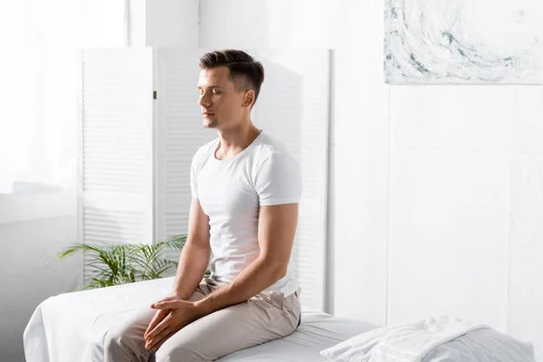 Man in white t-shirt sitting on massage table with closed eyes in clinic — Stock Photo