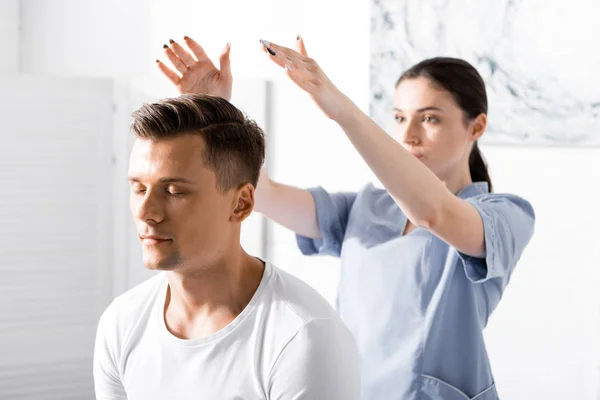 Man sitting with closed eyes while healer cleaning his aura — Stock Photo