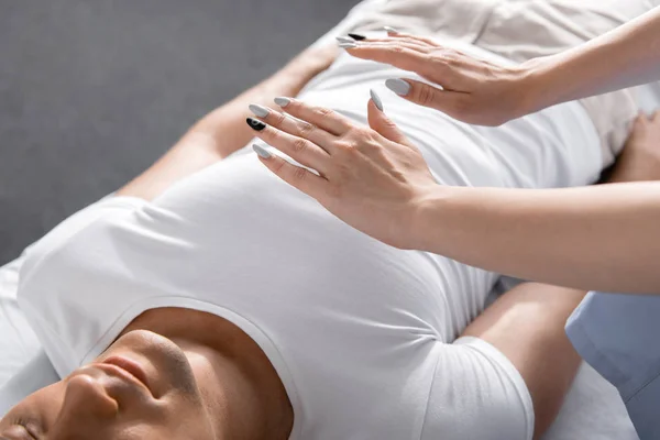 Teilansicht des Heilers, der neben einem Mann auf einem Massagetisch steht und die Hände über seinem Körper hält — Stockfoto