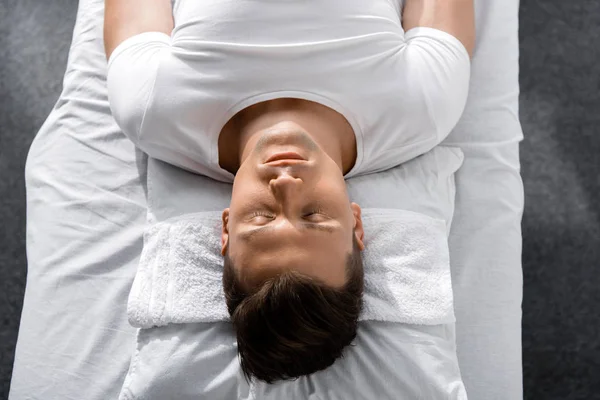 Jeune homme couché sur un oreiller sur une table de massage avec les yeux fermés — Photo de stock