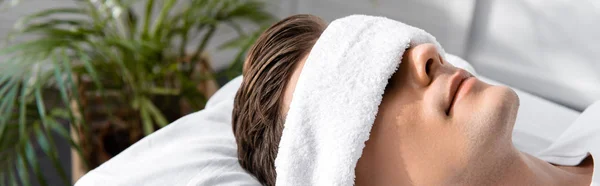 Panoramic shot of young man with towel on eyes lying on pillow — Stock Photo