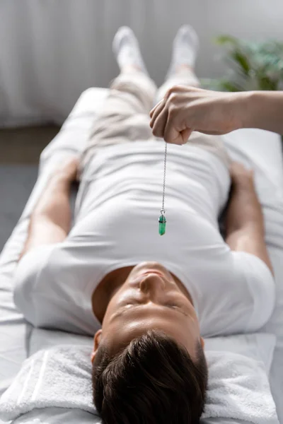 Cropped view of hypnotist standing near man on massage table and holding green stone — Stock Photo