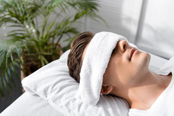 Young man with towel on eyes lying on pillow — Stock Photo