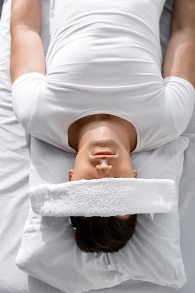 Vue de dessus du jeune homme avec serviette sur les yeux couché sur l'oreiller — Photo de stock