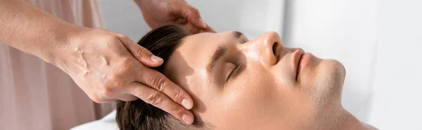 Panoramic shot of masseur standing near man with closed eyes and touching his head — Stock Photo