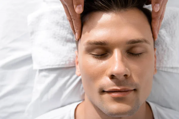 Cropped view of masseur standing near man with closed eyes and touching his head — Stock Photo