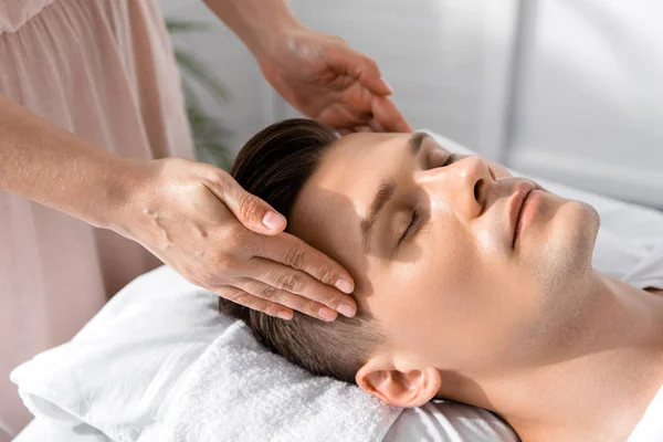 Cropped view of masseur standing near man with closed eyes and touching his head — Stock Photo