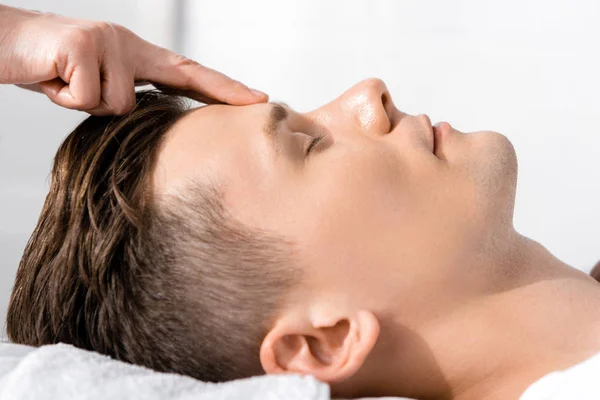 Cropped view of masseur standing near man with closed eyes and touching his forehead — Stock Photo