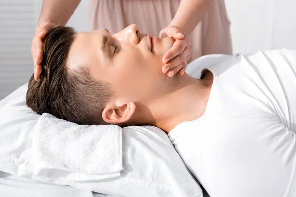 Ausgeschnittene Ansicht eines Masseurs, der mit geschlossenen Augen neben einem Mann steht und sein Gesicht berührt — Stockfoto