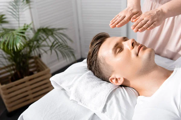 Cropped view of healer standing near man with closed eyes and holding hands above his head — Stock Photo