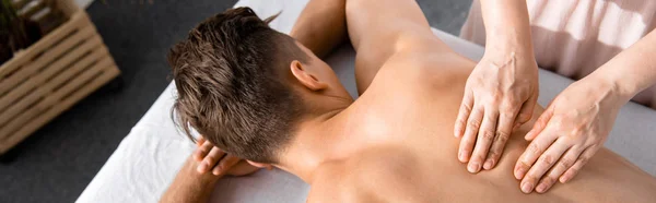 Panoramic shot of masseur and shirtless man lying on massage table — Stock Photo