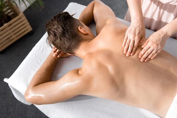 Vista recortada de masajista y hombre sin camisa acostado en la mesa de masaje - foto de stock