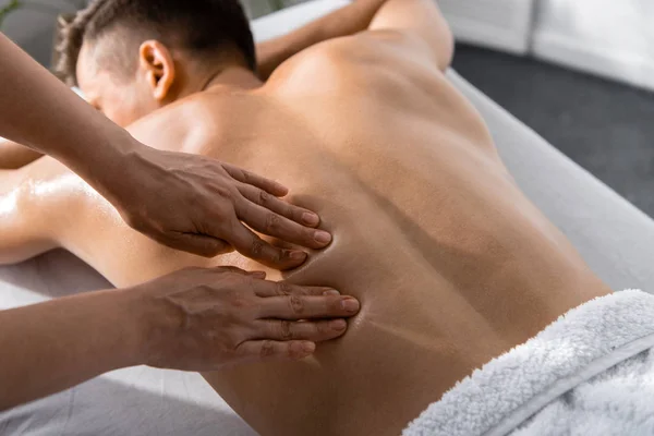 Vista recortada de masajista y hombre sin camisa acostado en la mesa de masaje - foto de stock