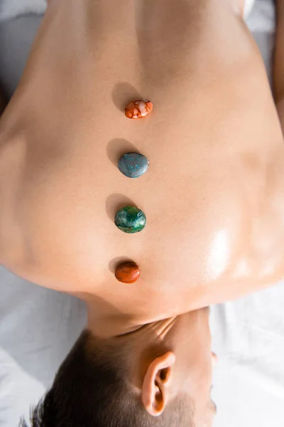 Vista recortada del hombre sin camisa acostado en la mesa de masaje con piedras en la espalda - foto de stock