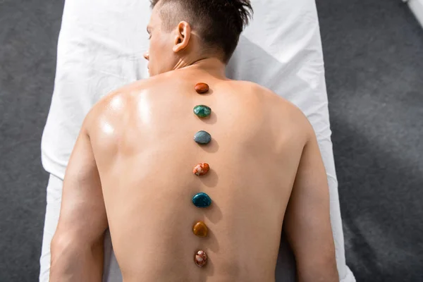 Top view of shirtless man lying on massage table with stones on back — Stock Photo