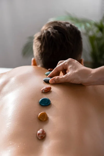 Cropped view of masseur and shirtless man with stones on back — Stock Photo