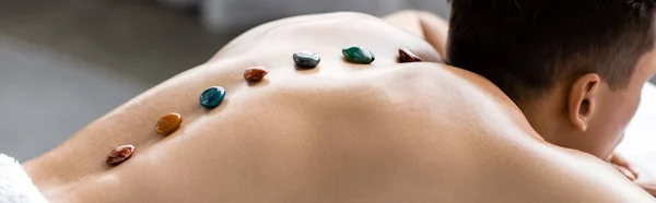 Panoramic shot of shirtless man with colorful stones on his back — Stock Photo