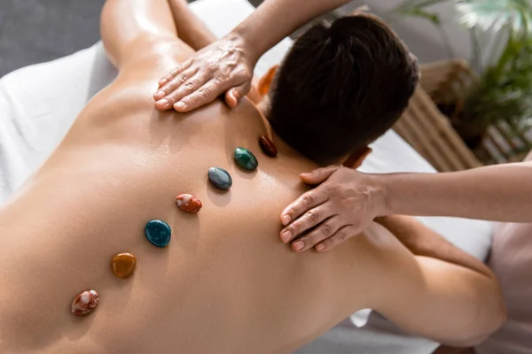 Cropped view of masseur and shirtless man with stones on back — Stock Photo