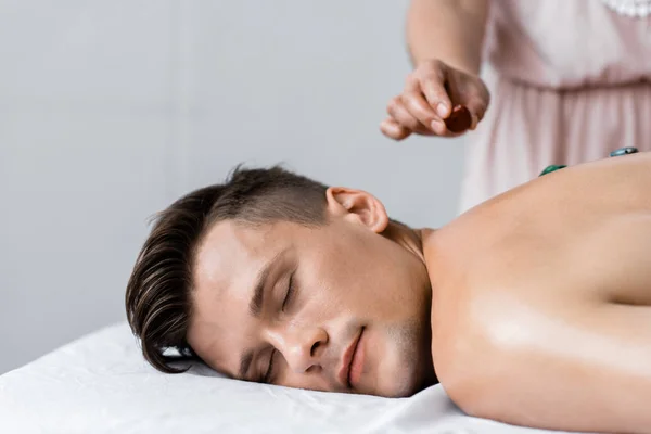 Cropped view of masseur and shirtless man with stones on back — Stock Photo