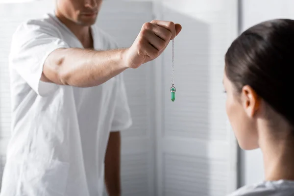 Cropped view of hypnotist standing near woman and holding green stone near her face — Stock Photo