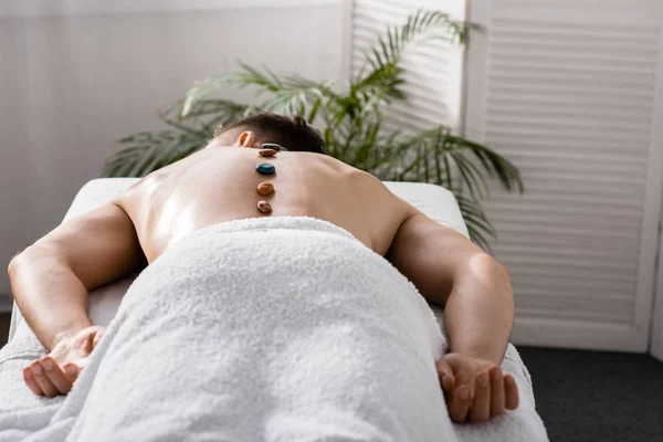 Hombre sin camisa acostado en la mesa de masaje con piedras en la espalda - foto de stock