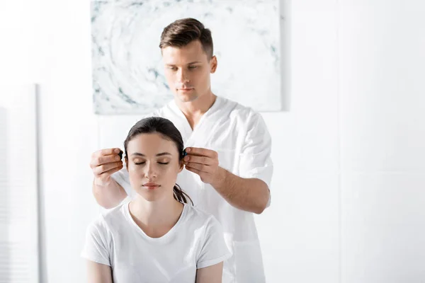 Guérisseur concentré debout près de la femme et tenant des pierres près de ses oreilles — Photo de stock