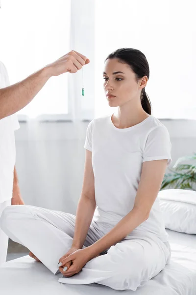 Cropped view of hypnotist standing near woman and holding green stone near her face — Stock Photo