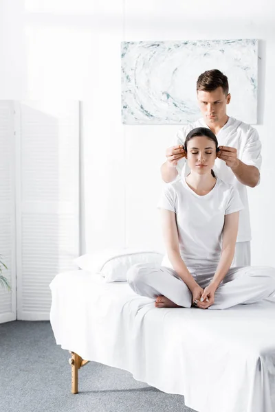 Woman sitting with closed eyes while healer holding stones near her ears — Stock Photo