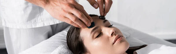 Prise de vue panoramique du guérisseur debout près de la femme avec les yeux fermés et en utilisant des pierres — Photo de stock